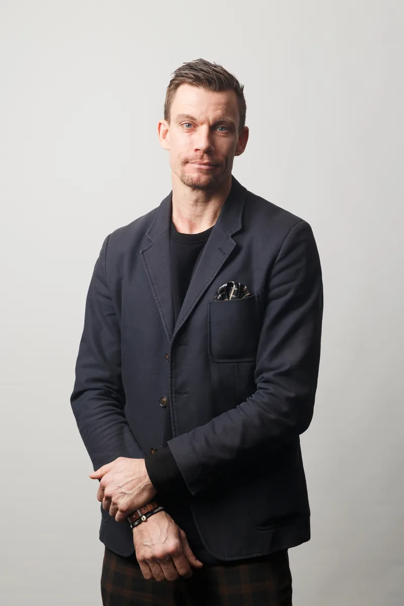 Rasmus Carlsson står mot en ljusgrå bakgrund, klädd i mörkblå kavaj och svart tröja.